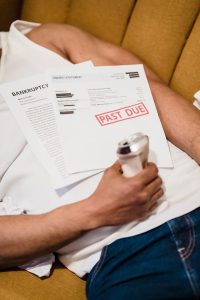Man holding bills labeled 'Past Due' and a drink can, lying on a sofa.