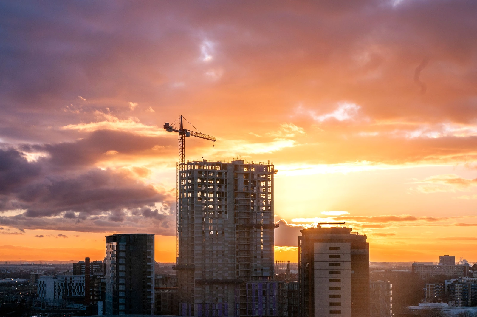 High-rise building under construction with tower crane at sunset